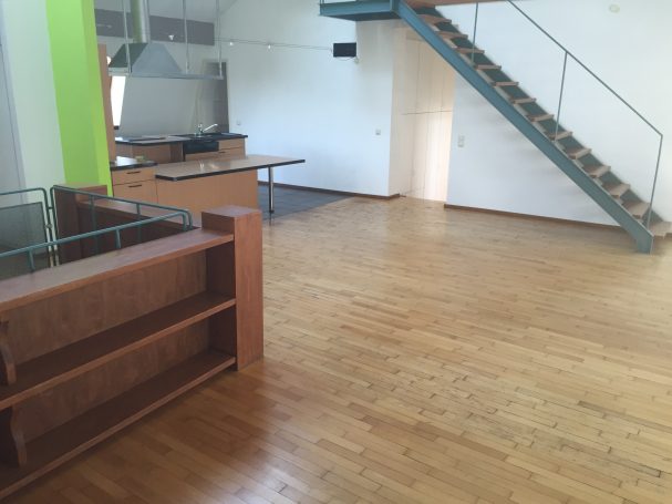 Innenraum mit Holzfußboden, offener Fläche und Treppe im Hintergrund.