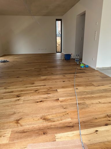 Helle, leere Zimmer mit Holzfußboden und offener Tür, Reinigungseimer und Spielzeug sichtbar.