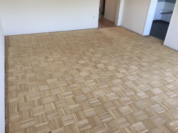 Boden mit hellen, schachbrettartigen Holzplatten in einem leeren Raum.