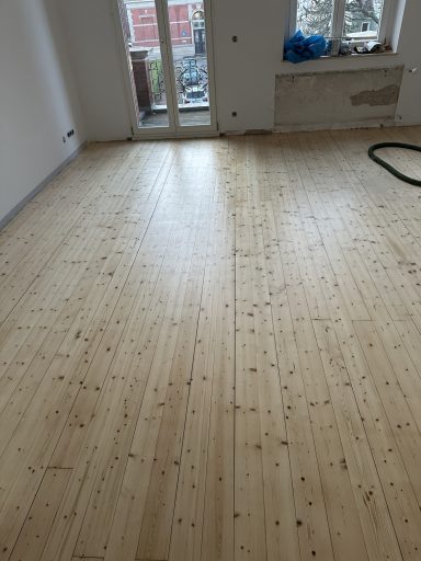 Heller Raum mit neu verlegtem Holzboden und Fenster mit Blick nach draußen.