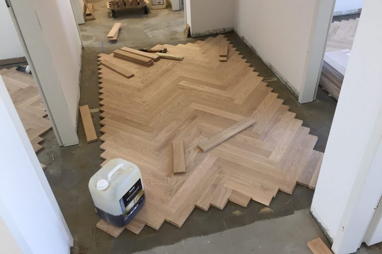 Holzboden im Fischgrätmuster, teilweise verlegt, mit Werkzeug und Materialien in der Nähe.