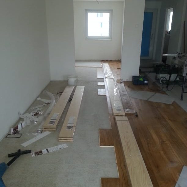 Unvollendeter Bodenbelag in einem Raum mit Holz- und Teppichmaterialien.