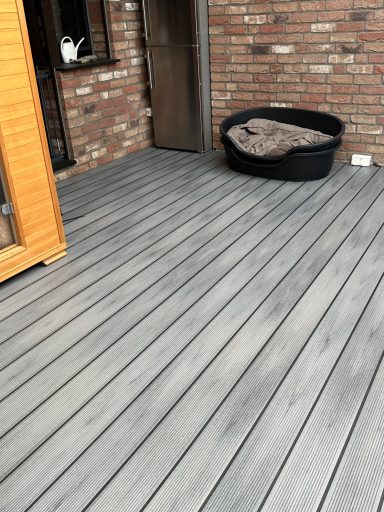 Holzterasse mit gebräuntem Boden, Korb mit Decke in der Ecke.