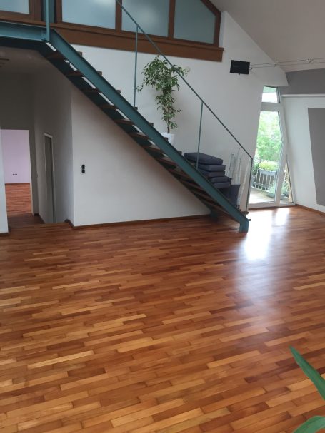 Holzboden in einem modernen Raum mit Treppe und großen Fenstern. Pflanzen dekorieren den Raum.