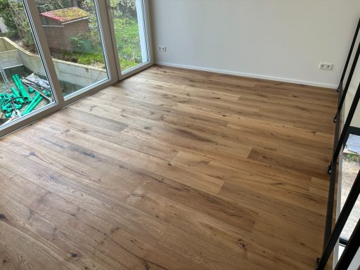 Holzboden in einem hellen Raum mit großen Fenstern und Blick ins Freie.