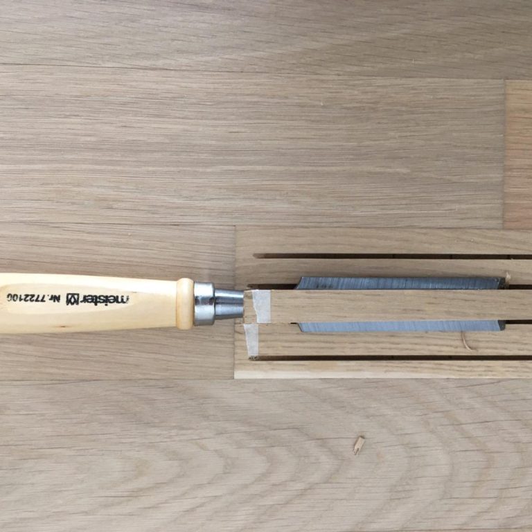 Holzbeitel mit Holzgriff liegt auf einer Holzoberfläche neben einem Holzstück.