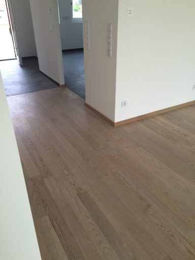 Helle, leere Räume mit Holzboden und grauen Fliesen im Hintergrund.