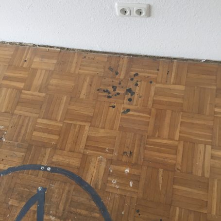 Holzboden mit Flecken und einer weißen Wandsteckdose.