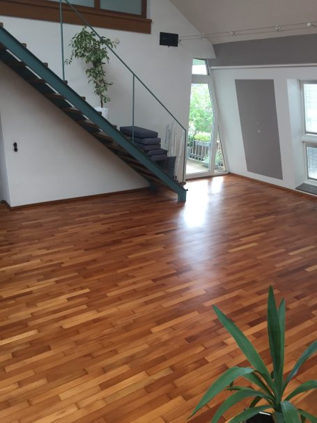 Helle Wohnung mit Holzfußboden, Treppe und großen Fenstern. Pflanzen dekorieren den Raum.