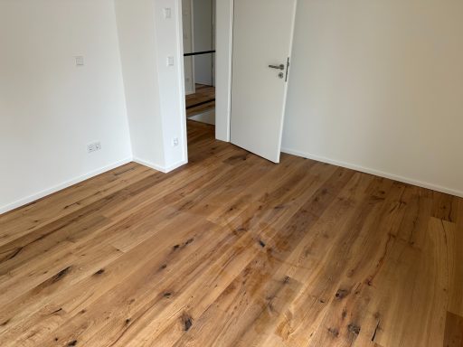 Heller Raum mit Holzfußboden und offener Tür zum angrenzenden Bereich.